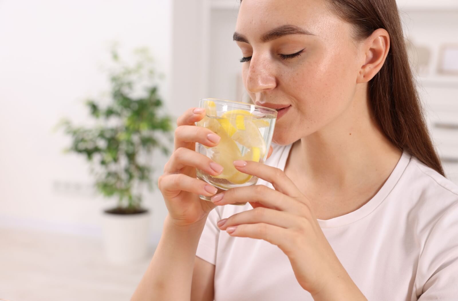 Relaxed woman holding a glass of sparkling water with lemon slices wearing a white top.