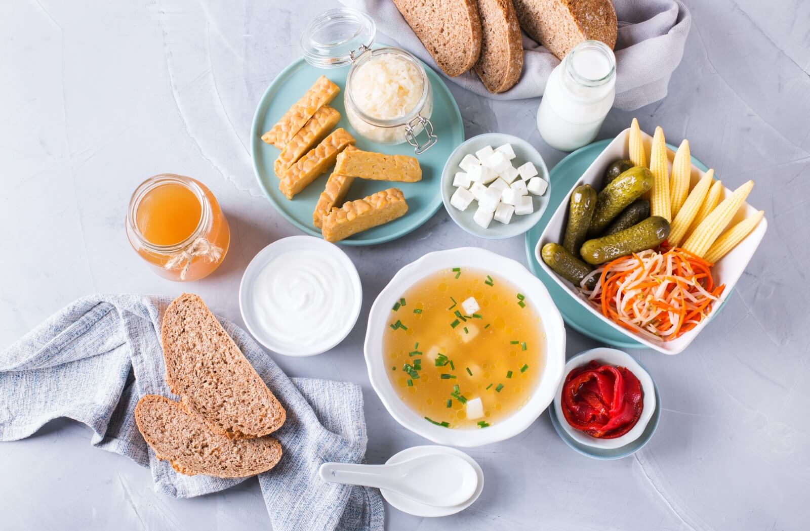 A platter of various healthy foods lay displayed on a table. A number of soft foods are included such as tofu, milk, yogurt, soup, honey and pickles.